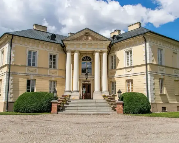 Elegancki pałac w Dobrzycy z kolumnowym portykiem i żółtą fasadą, otoczony zielenią.