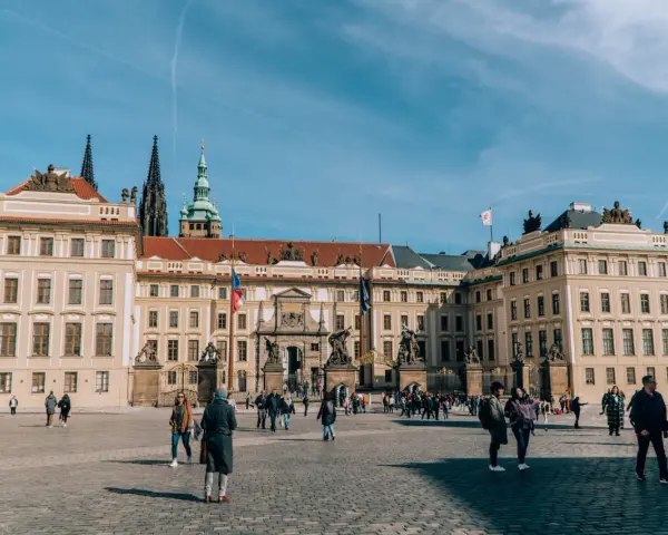 Tłum turystów spaceruje po dziedzińcu przed imponującym zamkiem na Hradczanach.