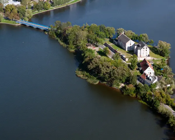 Ełk: zamek krzyżacki na wyspie, idealne miejsce na zwiedzanie. Most prowadzi do historycznych budynków otoczonych zielenią i wodą.