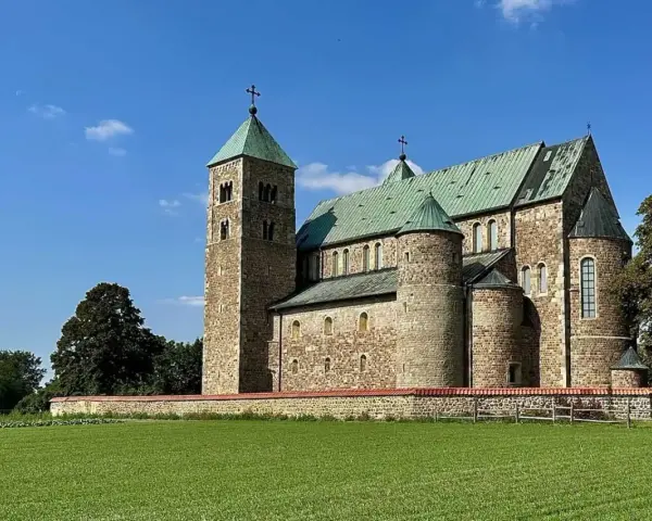 Kamienny zamek w Tumie z zielonym dachem, otoczony murem i zieloną łąką, pod błękitnym niebem.