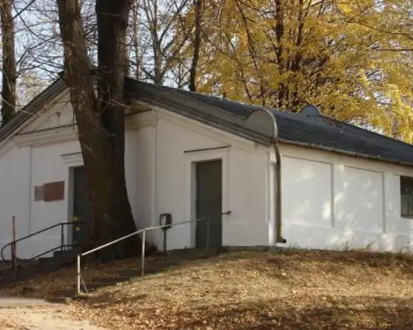 Ohel cadyka Elimelecha w Leżajsku zwiedzanie. Biały budynek z drzwiami i oknem, otoczony drzewami jesienią.