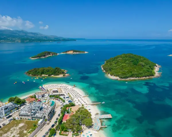 Albania Durrës atrakcje: malownicze wysepki z zieloną roślinnością otoczone turkusową wodą, plaża z leżakami i budynkami hotelowymi.