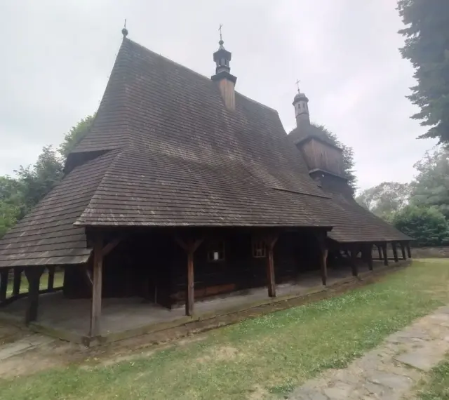 Drewniany kościół w Sękowej z charakterystycznym, wielospadowym dachem krytym gontem, otoczony zielenią.