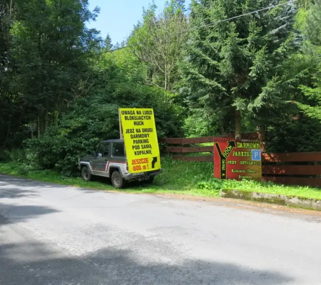 Samochód terenowy przy drodze, obok żółty znak informujący o darmowym parkingu przy sztolni kowary.