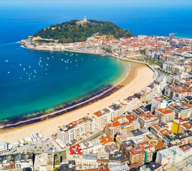 Widok z lotu ptaka na zatokę La Concha w San Sebastian, z piaszczystą plażą, turkusową wodą i zabudową miejską.