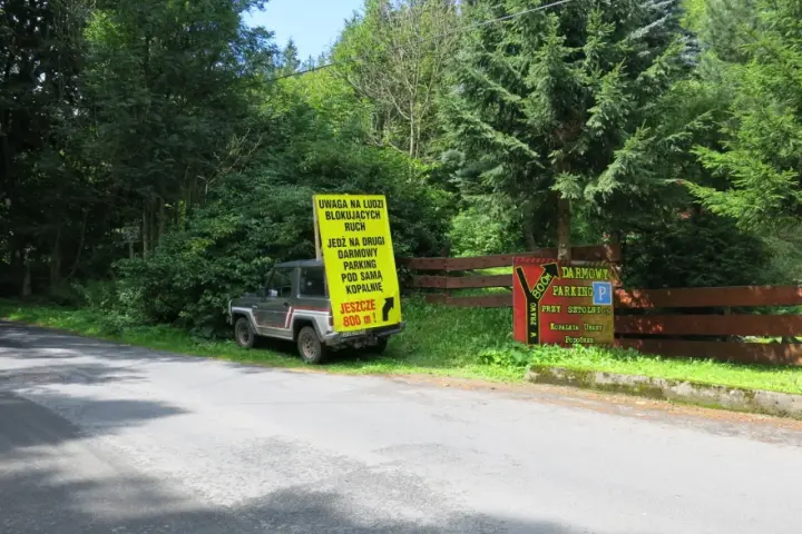 Samochód terenowy przy drodze, obok żółty znak informujący o darmowym parkingu przy sztolni kowary.
