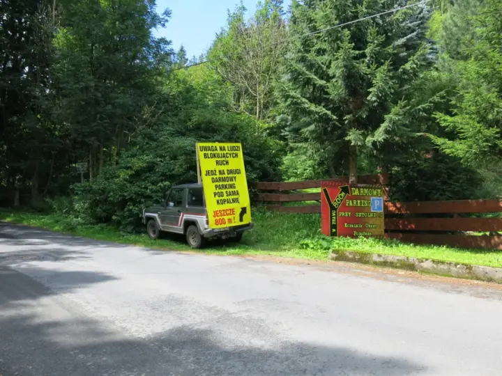 Samochód terenowy przy drodze, obok żółty znak informujący o darmowym parkingu przy sztolni kowary.
