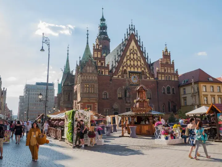 Tłum ludzi spaceruje po starym rynku we Wrocławiu, podziwiając piękną architekturę i letnie stoiska.
