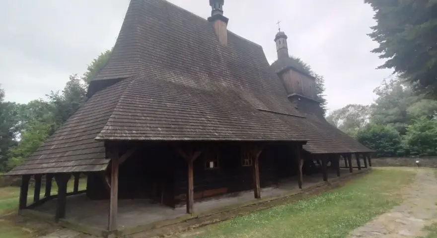 Drewniany kościół w Sękowej z charakterystycznym, wielospadowym dachem krytym gontem, otoczony zielenią.