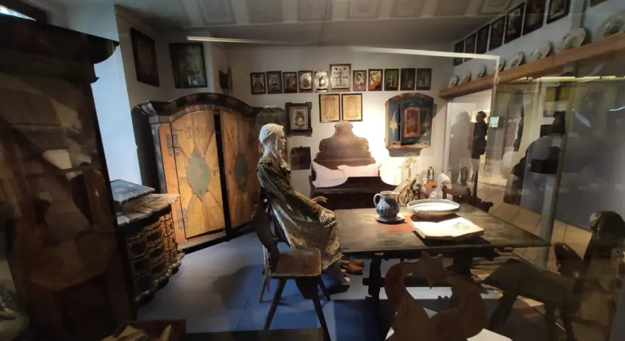 Wrocław Muzeum Etnograficzne: ekspozycja dawnej izby z manekinem w stroju ludowym, zdobionymi meblami i obrazami na ścianach.