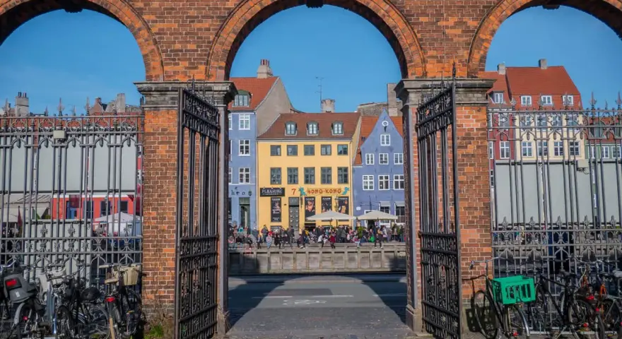 Kolorowe kamienice nad kanałem, idealne na szybkie zwiedzanie Kopenhagi w jeden dzień. Rowerzyści czekają na przejazd.