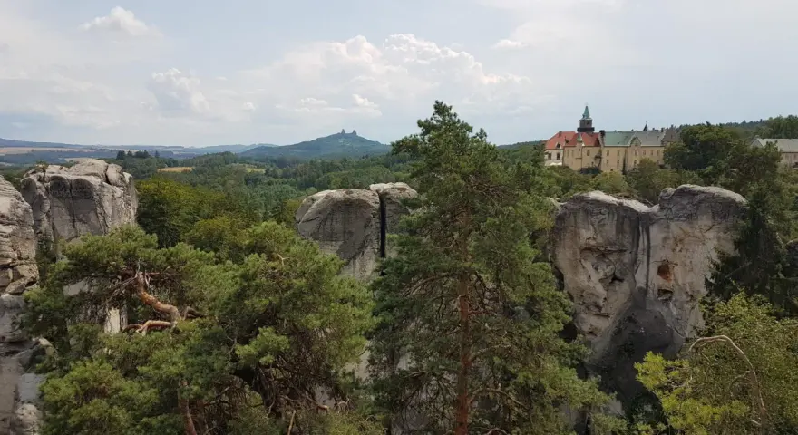 Widok na zamek Hrubá Skála otoczony skalnymi formacjami i lasem.