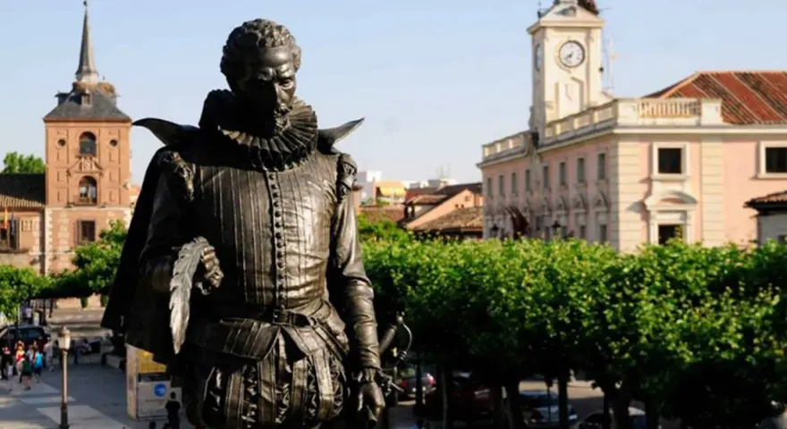 Pomnik Cervantesa w Alcalá de Henares, z ratuszem i wieżą zegarową w tle.
