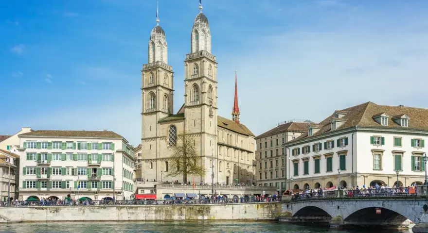 Zurych co warto zobaczyć: imponująca katedra Grossmünster z dwiema wieżami, rzeka Limmat i most.