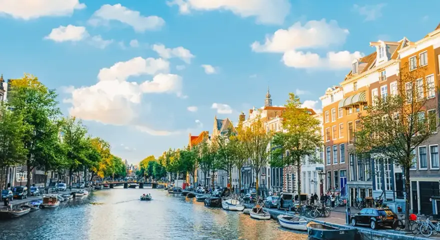 Widok na kanał w Amsterdamie, z łodziami, kamienicami i zielenią. Idealne miejsce na spacer, gdzie jest Amsterdam.