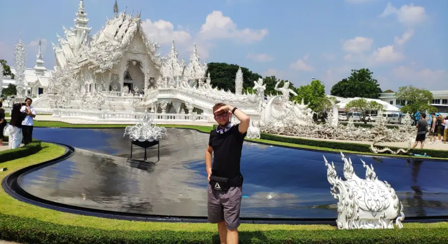 Mężczyzna pozuje przed olśniewającą białą świątynią Wat Rong Khun w Chiang Rai.