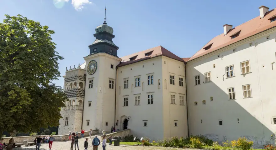 Zamek w Pieskowej Skale z charakterystyczną wieżą zegarową i renesansową attyką. Zwiedzający spacerują po dziedzińcu.