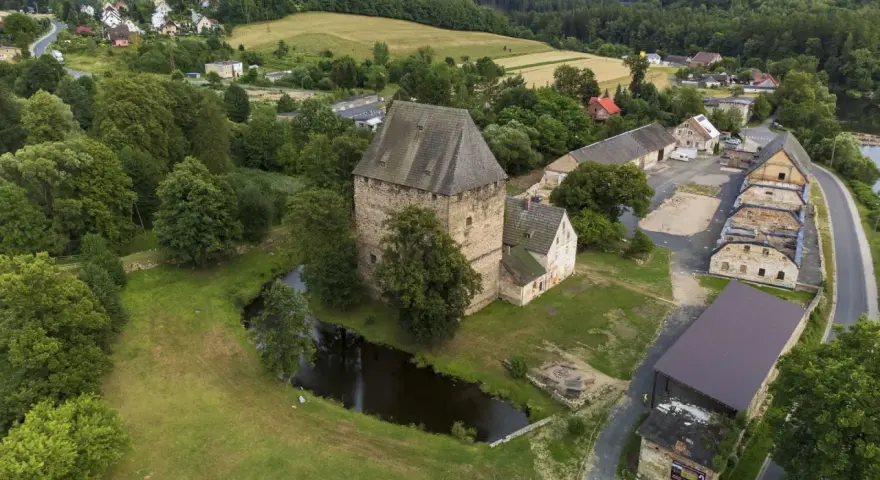 Wieża w Siedlęcinie, otoczona zielenią i stawem, góruje nad okolicą. W tle widać zabudowania i pagórkowaty krajobraz.