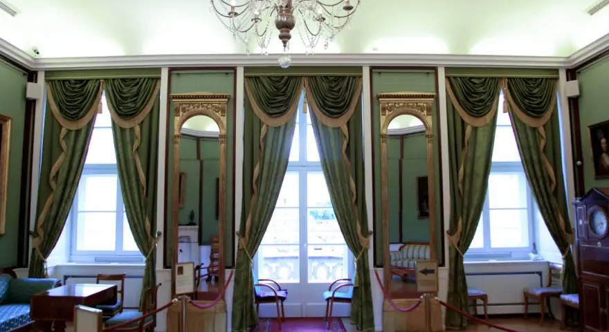 Wnętrze pałacu królewskiego we Wrocławiu. Eleganckie zielone zasłony, złote lustra i kryształowy żyrandol tworzą atmosferę dawnej świetności.