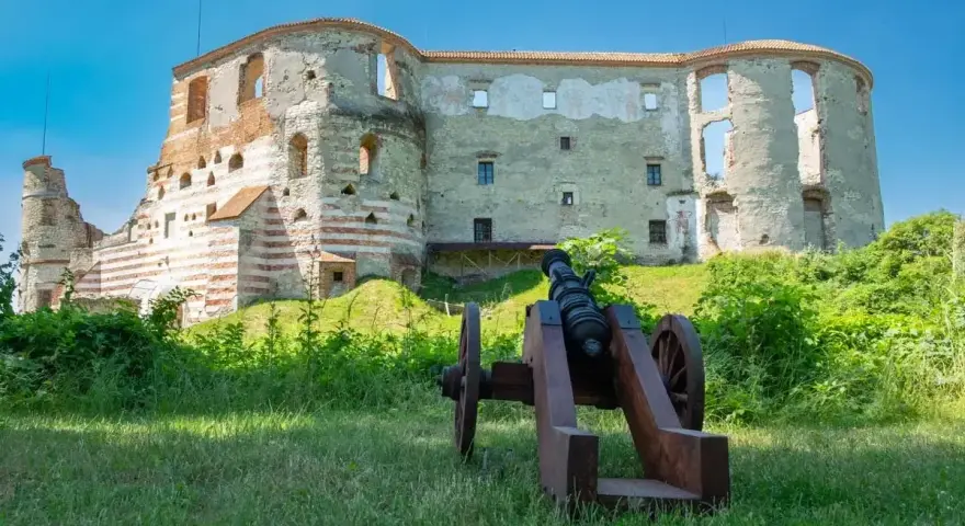 Zamek w Janowcu, ruiny warowni z armatą na pierwszym planie, pod błękitnym niebem.