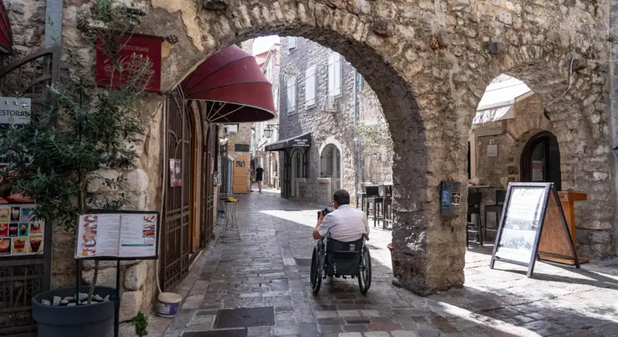 Mężczyzna na wózku inwalidzkim przemierza urokliwe, kamienne uliczki **Budva stare miasto**.
