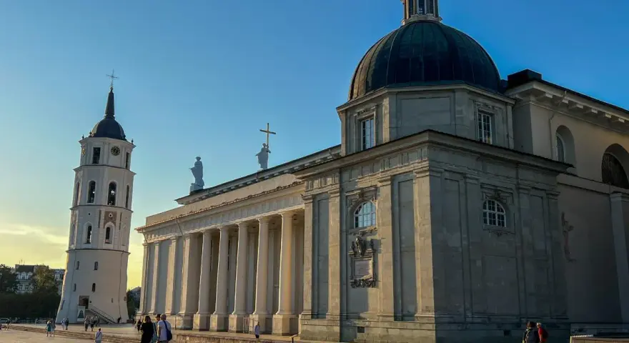Wileńskie kościoły: Katedra i dzwonnica na placu. Słońce oświetla monumentalną architekturę, tworząc długie cienie.