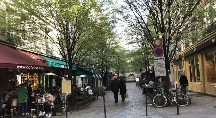 Spacerem w le Marais, Paryż, z kawiarniami i ludźmi spacerującymi pod drzewami.