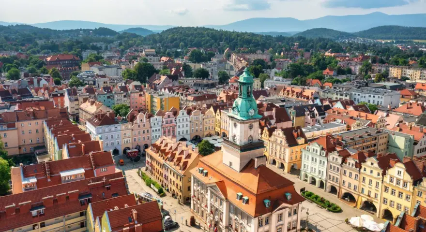 Widok z lotu ptaka na kolorowy rynek starego miasta z wieżą ratuszową i górzystym tłem.