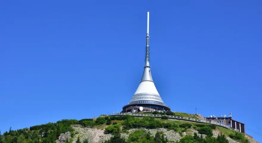 Wieża telewizyjna Ještěd, jedna z głównych libereckich atrakcji, góruje nad zielonym wzgórzem pod błękitnym niebem.