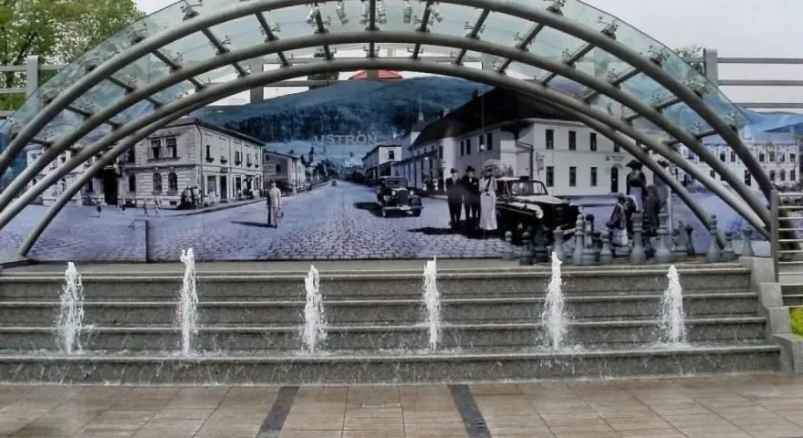 Ustroń rynek: fontanna i mural przedstawiający historyczne miasto z ludźmi w strojach z epoki i zabytkowymi samochodami.