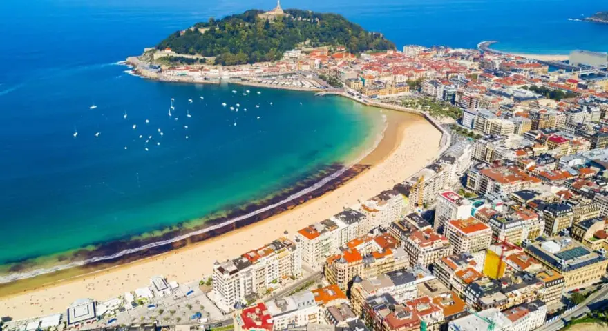 Widok z lotu ptaka na zatokę La Concha w San Sebastian, z piaszczystą plażą, turkusową wodą i zabudową miejską.