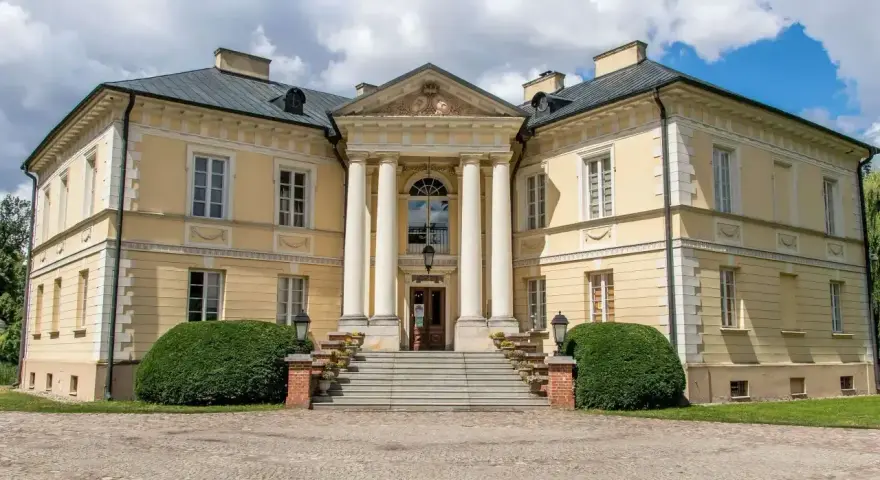 Elegancki pałac w Dobrzycy z kolumnowym portykiem i żółtą fasadą, otoczony zielenią.