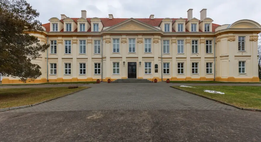 Pałac biskupów kujawskich w Wolborzu, okazała budowla z żółtą fasadą i czerwonym dachem, otoczona zielenią i brukowanym podjazdem.