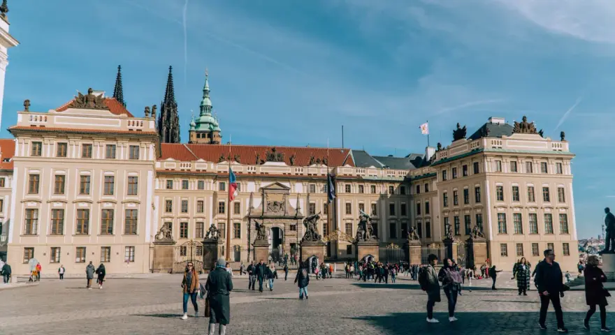 Tłum turystów spaceruje po dziedzińcu przed imponującym zamkiem na Hradczanach.