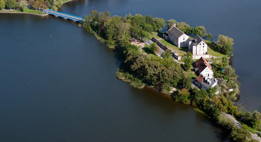 Ełk: zamek krzyżacki na wyspie, idealne miejsce na zwiedzanie. Most prowadzi do historycznych budynków otoczonych zielenią i wodą.