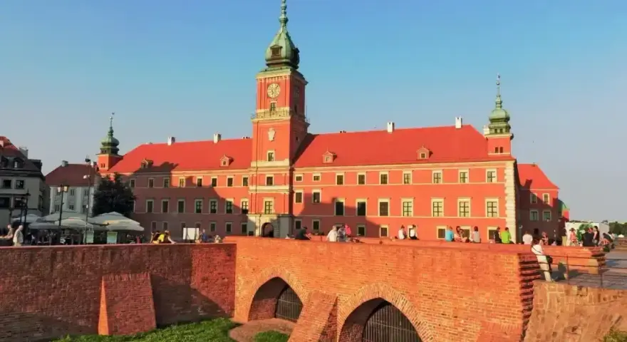 Słoneczny dzień na placu zamkowym w Warszawie. Ludzie odpoczywają na murze przy Zamku Królewskim.