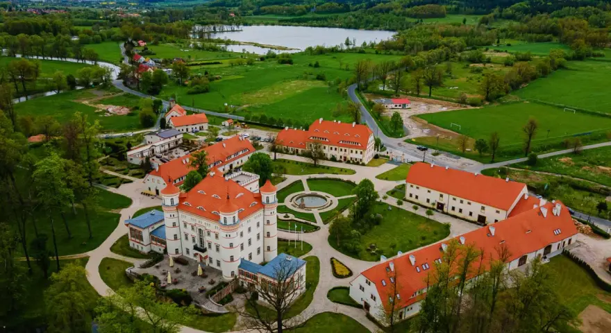 Pałac w Wojanowie otoczony zielenią, z jeziorem w tle. Malowniczy widok z lotu ptaka na zabytkową architekturę i otaczający krajobraz.