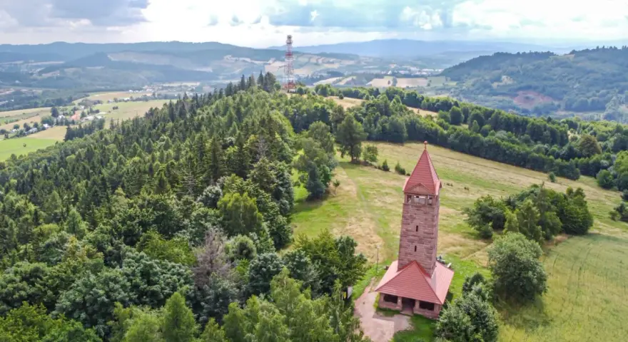 Wieża widokowa w górach zaprasza na podziwianie krajobrazu. W oddali widać maszt telekomunikacyjny.