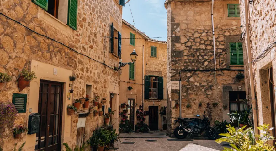 Urokliwa uliczka w Valldemossa. Zobacz kamienne domy z zielonymi okiennicami i mnóstwo kwiatów. Idealne miejsce na spacer i odkrywanie uroków miasteczka.