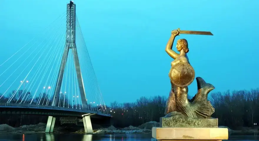 Syrenka warszawska z mieczem i tarczą stoi nad Wisłą, w tle nowoczesny most.