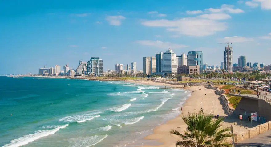 Słoneczna tel aviv plaża z turkusową wodą i nowoczesnymi wieżowcami w tle.