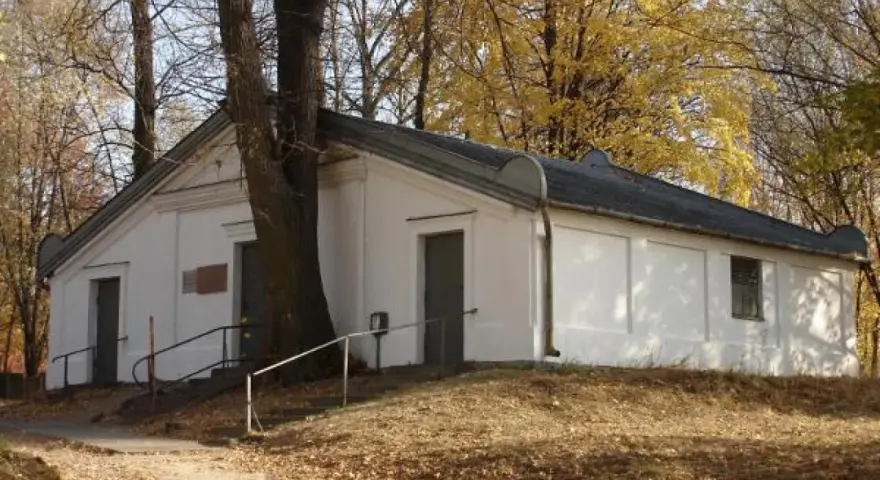 Ohel cadyka Elimelecha w Leżajsku zwiedzanie. Biały budynek z drzwiami i oknem, otoczony drzewami jesienią.