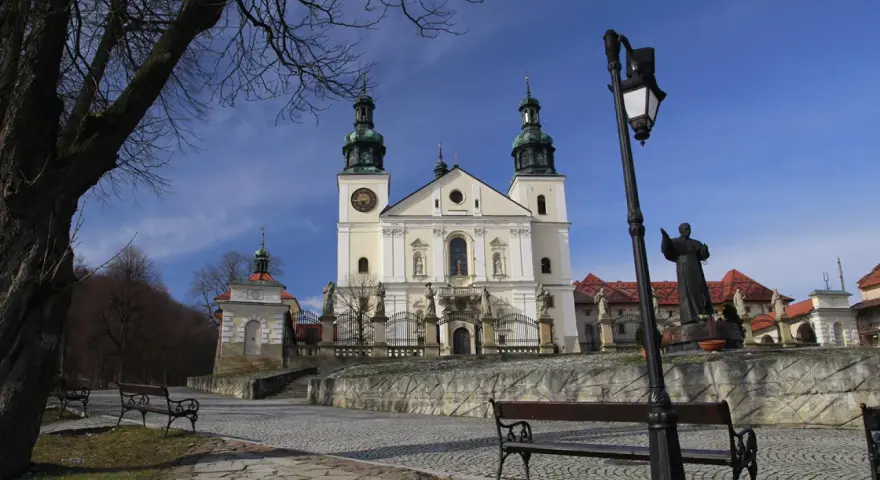 Kalwaria Zebrzydowska zwiedzanie: barokowy kościół z wieżami, kapliczki, ławki i pomnik.