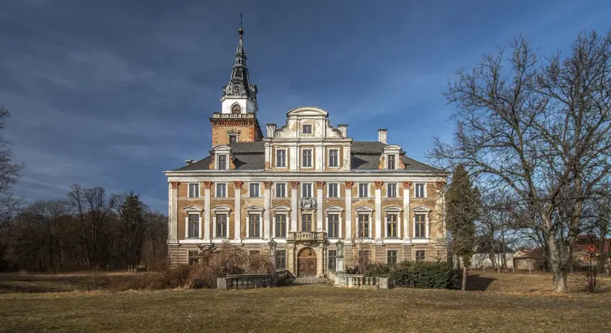Imponujący zamek w Roztocze, z charakterystyczną wieżą i bogato zdobioną fasadą, otoczony parkiem.