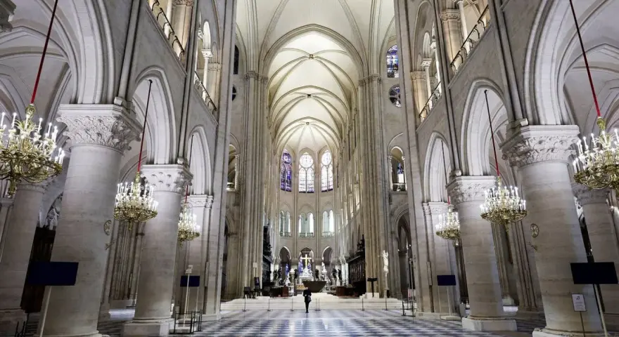 Wnętrze katedry Notre Dame, z monumentalnymi kolumnami, sklepieniem i witrażami. Na środku nawy stoi samotna postać.