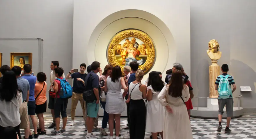 Galeria Uffizi: co zobaczyć? Grupa turystów podziwia okrągły obraz w złotej ramie i rzeźbę.