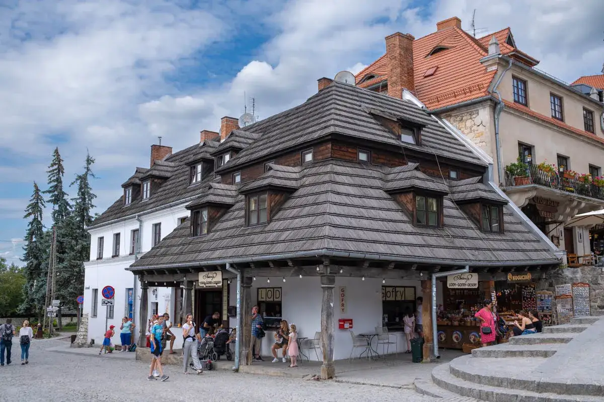 Kazimierz Dolny rynek tętni życiem. Ludzie spacerują, kupują lody i gofry pod urokliwymi, drewnianymi dachami kamienic.