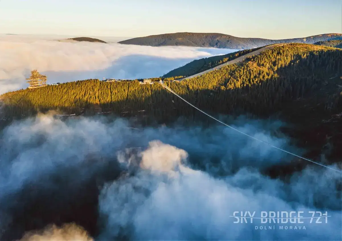 Widok na wiszący most Sky Bridge 721 w Doln&iacute; Moravě, otoczony chmurami i lasem.