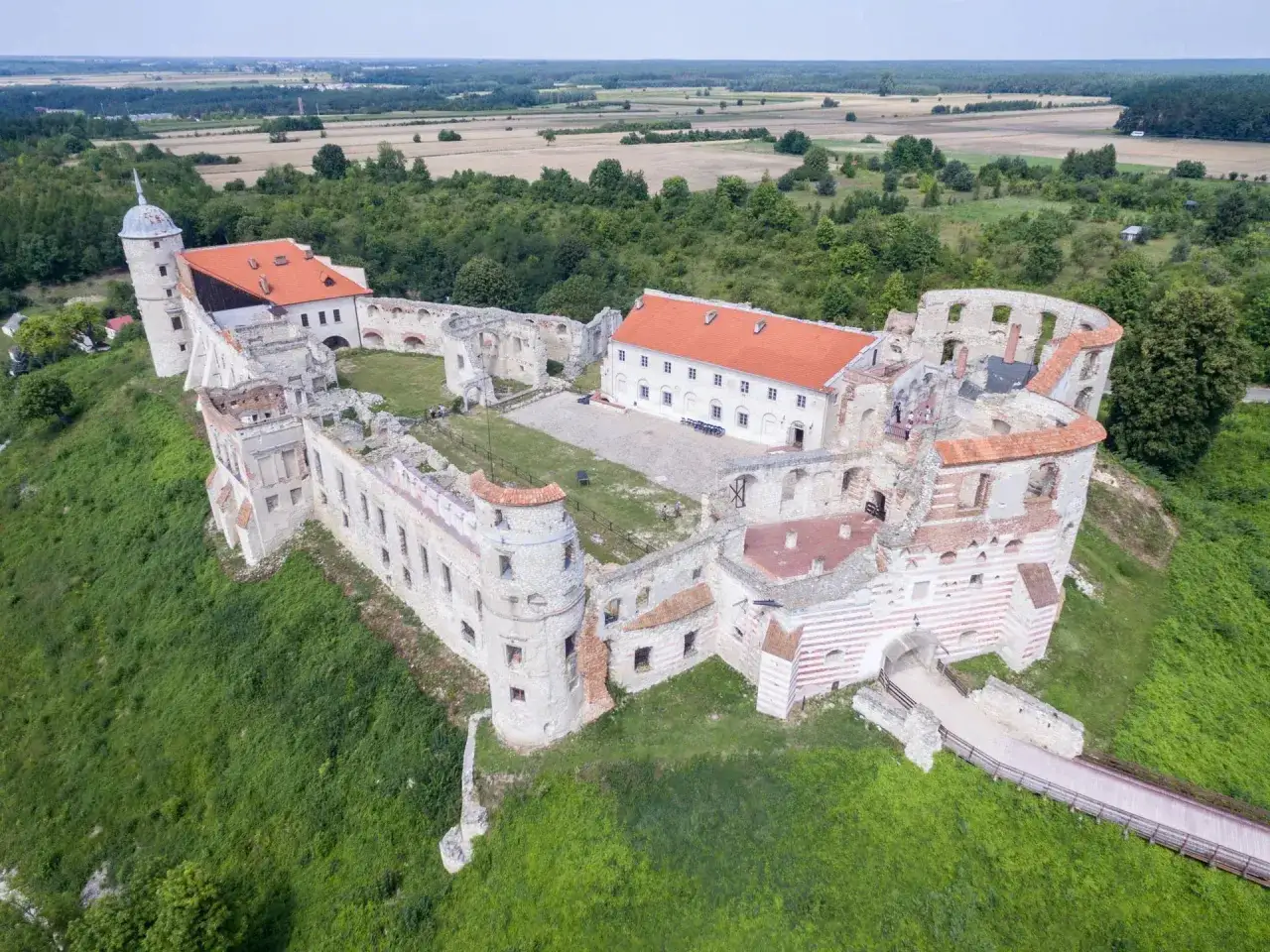 Ruiny zamku na wzgórzu, z widokiem na pola i lasy.