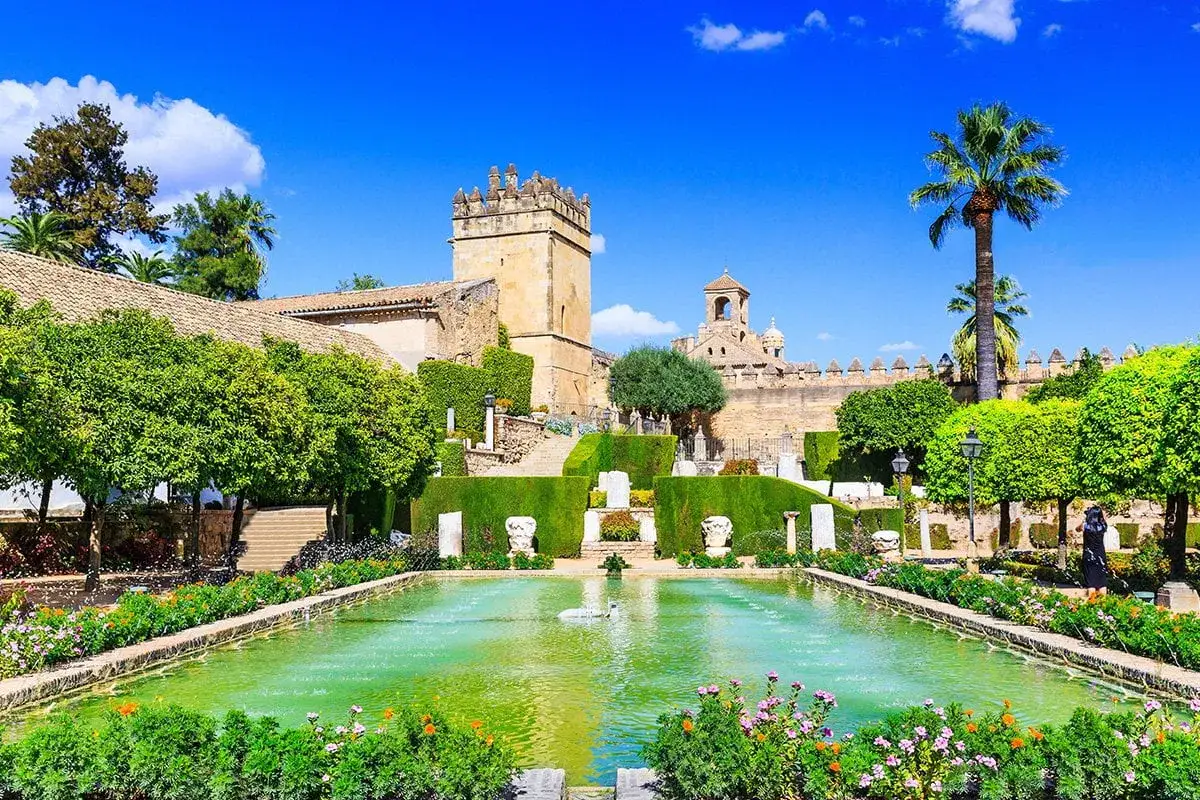 Kordoba co zobaczyć: malowniczy ogród z basenem i fontanną, otoczony zielenią i zabytkową architekturą.